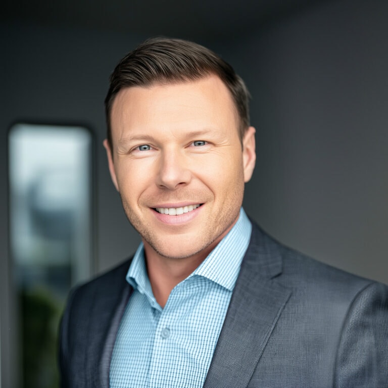 A1: A professional man with short brown hair, blue eyes, and a friendly smile, wearing a dark gray suit and light blue shirt, standing indoors with a blurred background.